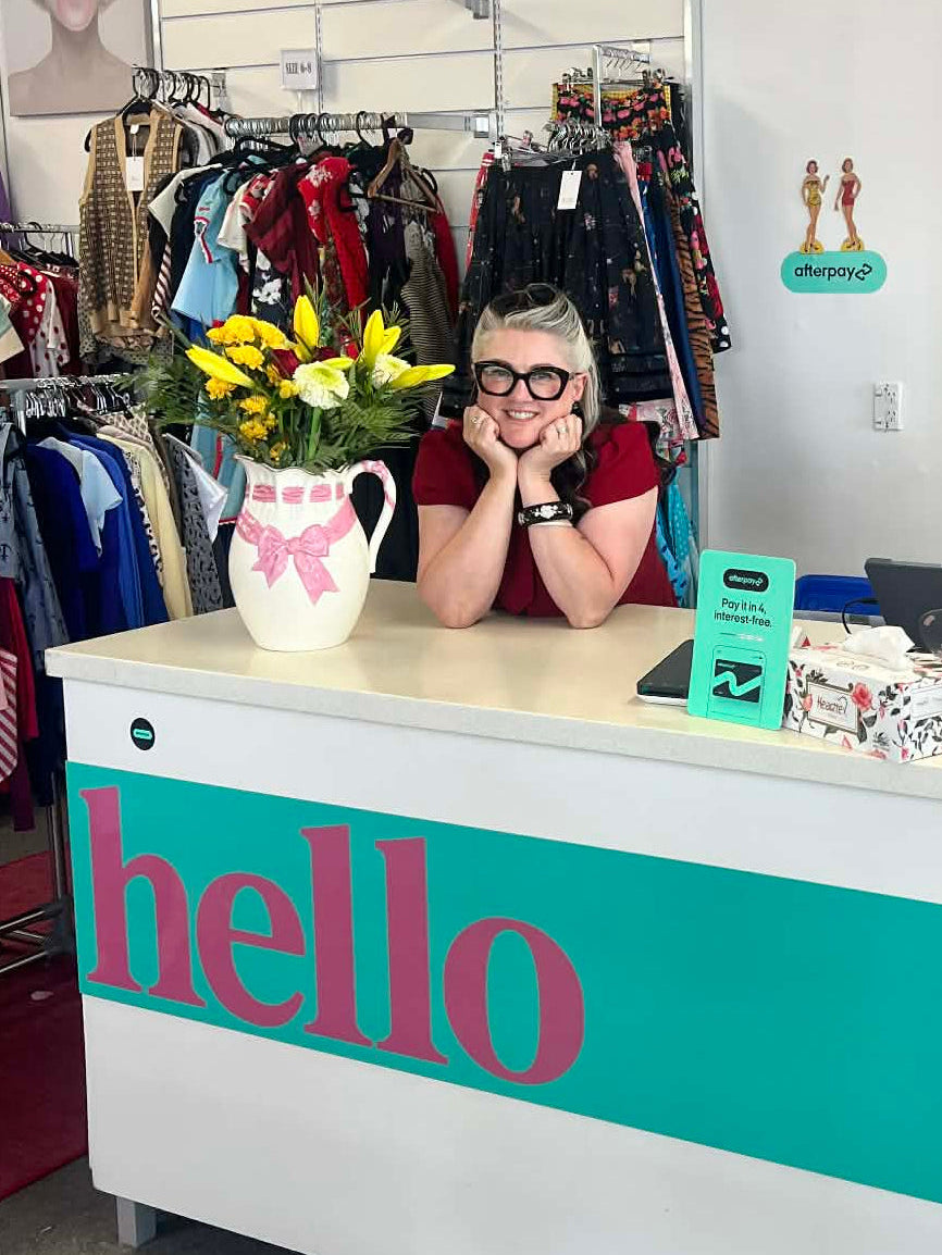 Person sitting behind a counter with 'hello' sign in a store setting